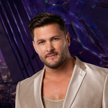 Brock Davies Wears a gold blazer and tank top while in a purple room overlooking LA.