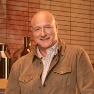 Tom Colicchio wearing a brown top in a food pantry