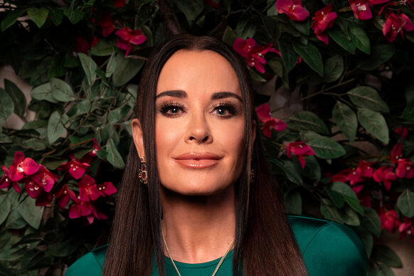 Kyle Richards wearing a silk, green, gown in front of a Beverly Hills inspired set.