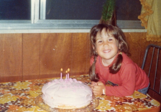Jacqueline Laurita as a child posing on a table with a birthday cake.