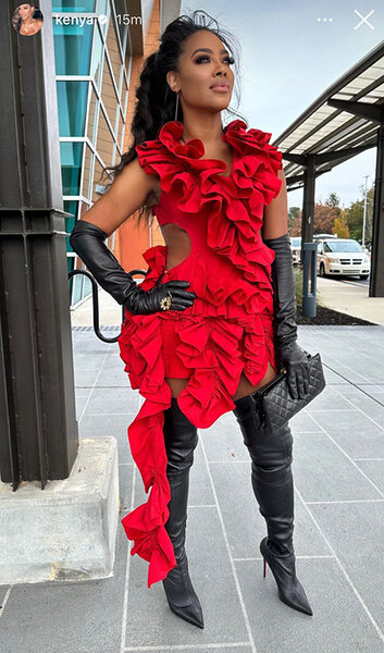 Kenya posing on a sidewalk in a bright red, ruffled, mini dress with an updo, black leather gloves, and black thigh high boots.