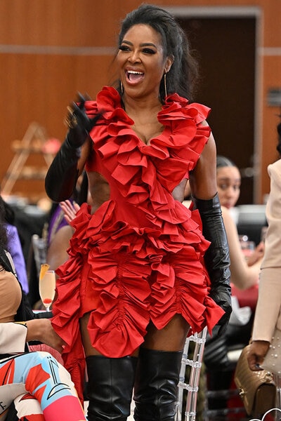 Kenya smiling in a bright red, ruffled, mini dress with black leather gloves and boots.