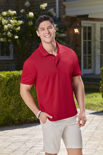 Alex Wach wearing a red polo and khaki shorts in front of a house.
