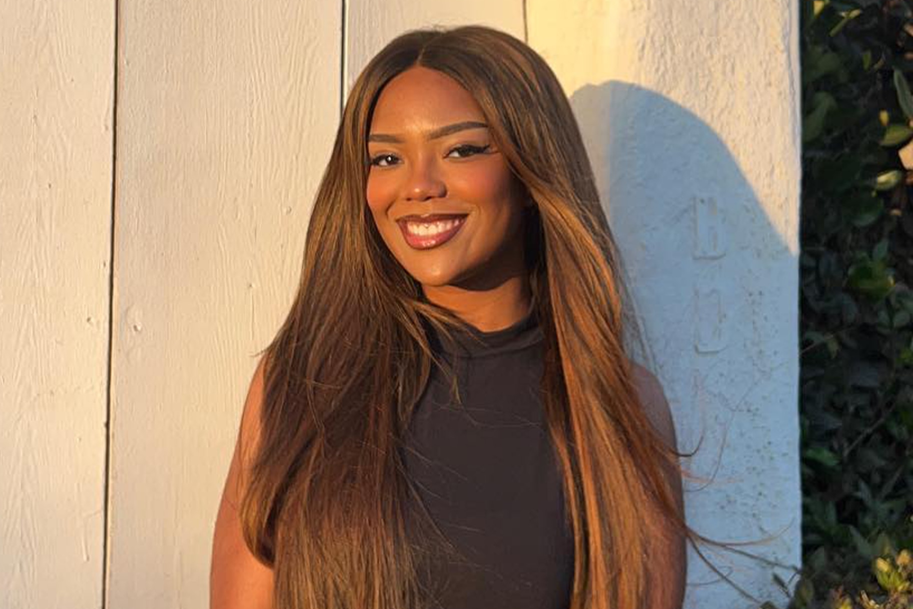 Riley Burruss smiling in a black outfit in front of a wooden, white, door.