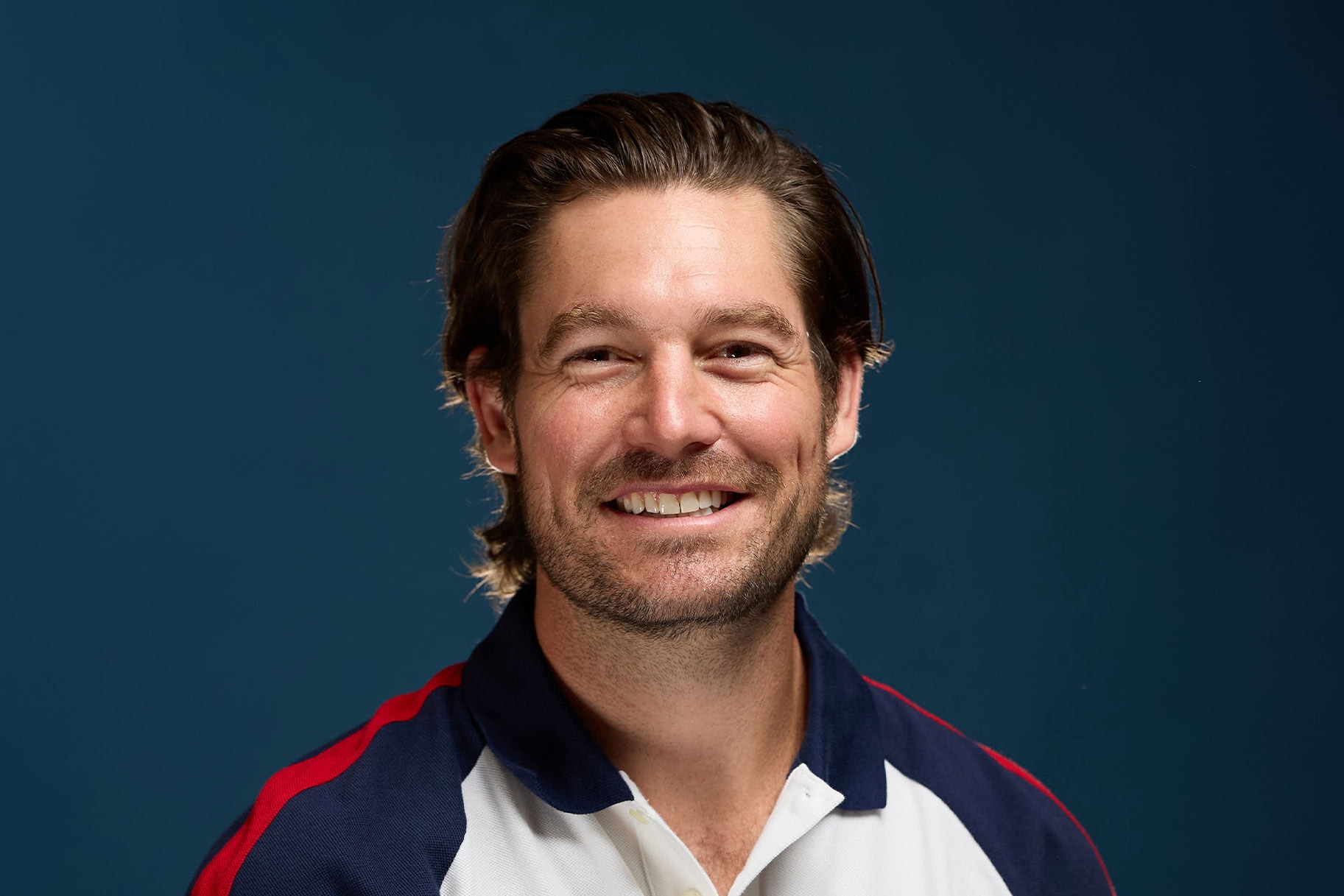 Craig Conover smiling in front of a blue background.