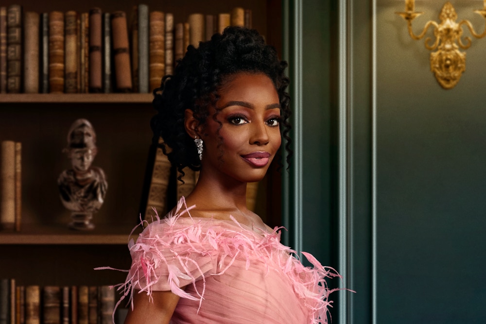 Venita Aspen wearing a pink dress standing in front of a book shelf