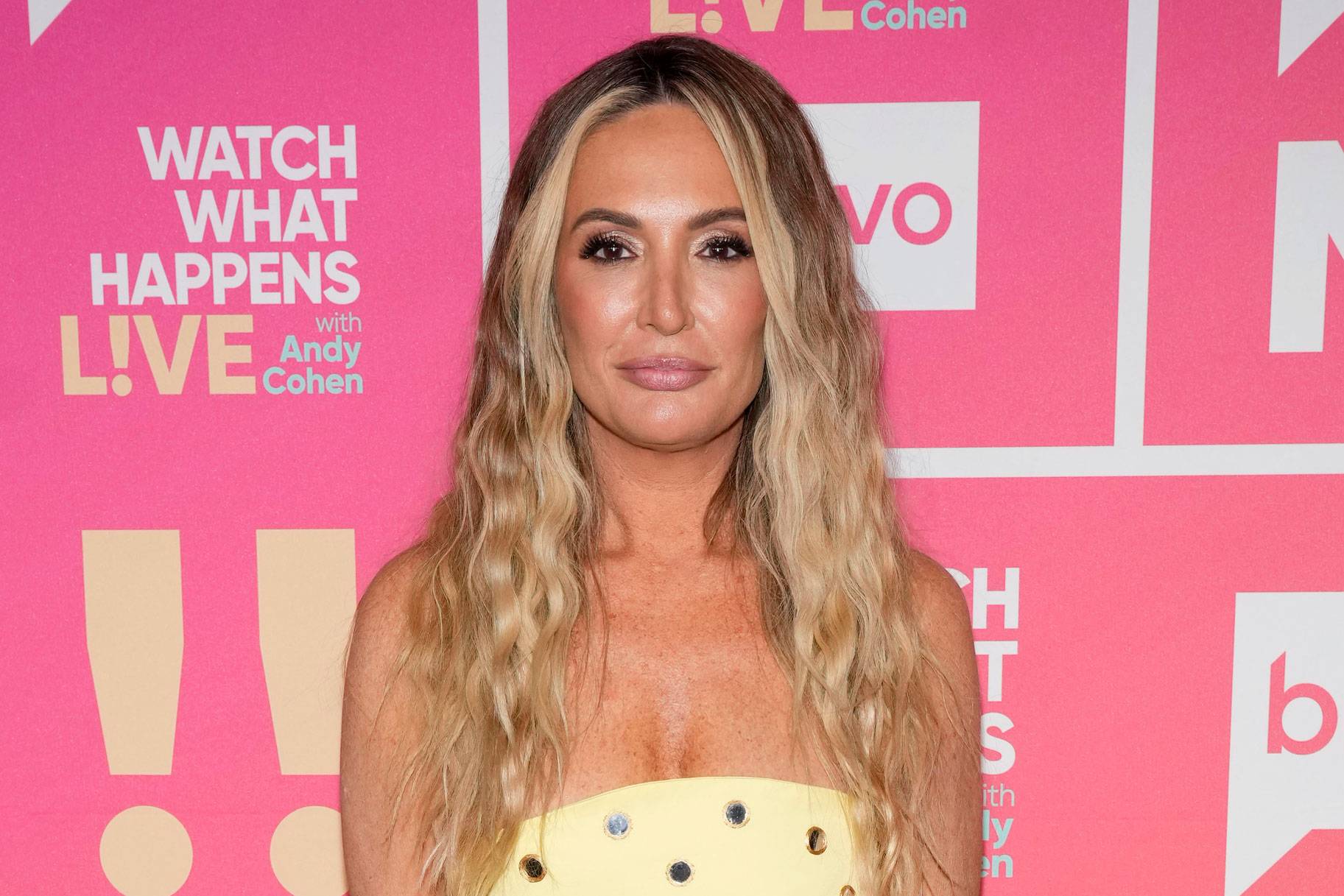 Kate Chastain wearing a yellow strapless dress in front of a WWHL step and repeat.