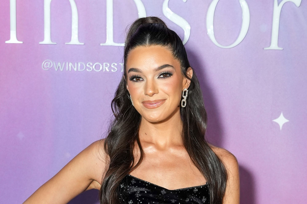 Ally Lewber wearing a black dress in front of a purple step and repeat on NYE