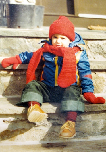 Josh Altman sitting on steps in a winter coat and mittens as a child