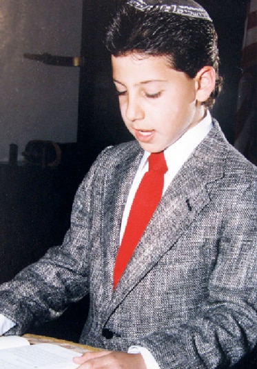 A young Josh Altman reads from a book in a gray suit