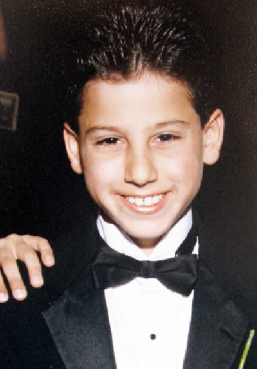 A young Josh Altman from MDLLA smiling wearing a tuxedo with a hand on his shoulder