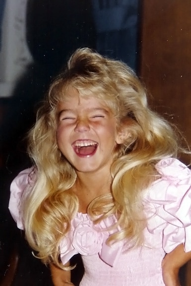 Heather Altman as a child laughing while wearing a pink frilly dress