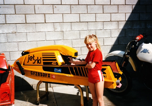 Gretchen Rossi as a child standing next to a jet-ski.