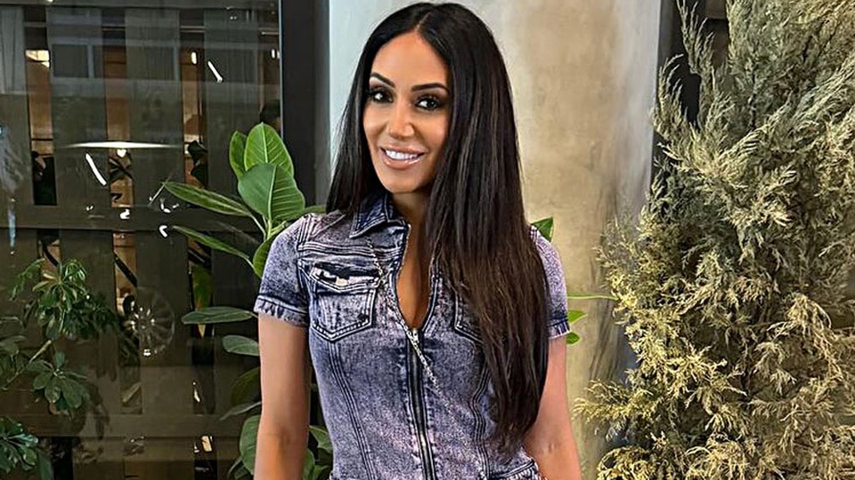 Melissa Gorga wears a denim onsie while standing in front of greenery