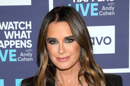 Kyle Richards with smokey eye makeup standing in front of the Watch What Happens Live step and repeat