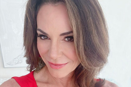 Luann in a red outfit in front of a white wall.