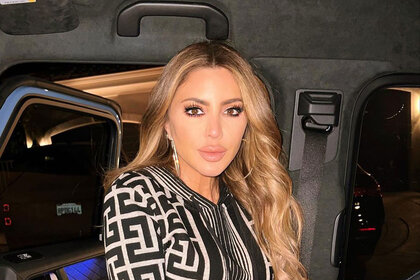 Larsa with her hair down in a patterned black and nude dress inside of a car.