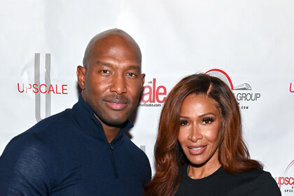 Martell Holt and Sheree Whitfield pose together in front of a step and repeat.