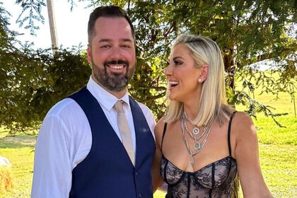 Gina Kirschenheiter and Travis Mullen smiling together outside underneath a large tree.