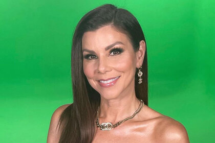 Heather Dubrow smiling in front of a green screen.