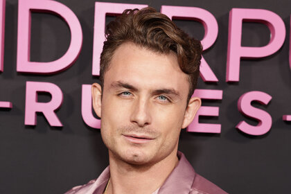 James Kennedy in front of a step and repeat at an event wearing a pink, collared, shirt.