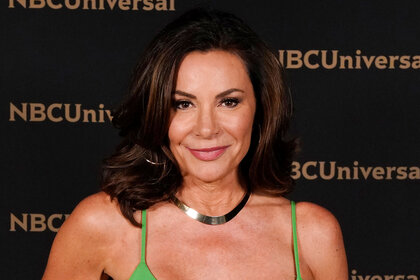 Luann in a neon green dress in front of a step and repeat.