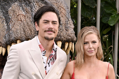 Tom Sandoval and Ariana Madix pose in front of a realistic, large scale, dinosaur head together.