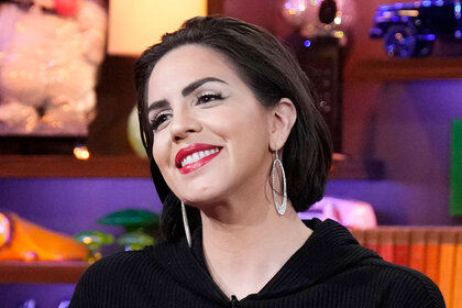 Katie smiling with red lipstick and a black hoodie in the WWHL clubhouse.