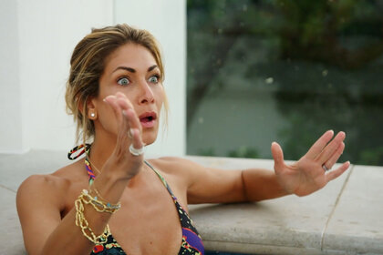 Erin in the pool wearing a bikini looking upset.