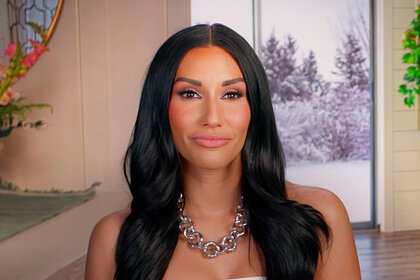 Monica Garcia smirking in a white top and silver necklace.