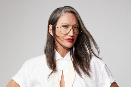 Jenna Lyons wearing a white button up top in front of a grey backdrop