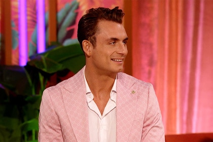 James Kennedy smiling in a pink suit in front of plants and curtains.