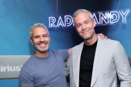 Andy Cohen and Ryan Serhant posing next to each other in front of a neon sign.