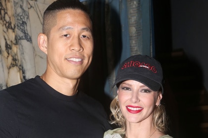 Ariana Madix and Daniel Wai smiling together in front of a marble wall.