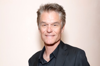 Harry Hamlin wearing a black suit in front of a beige backdrop