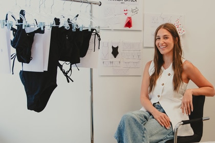 Amanda Batula sitting next to swimsuits she designed for her new swim line