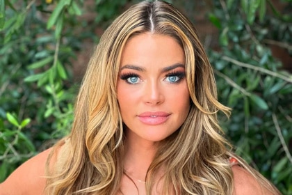 Denise Richards posing in front of foliage.