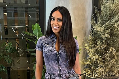 Melissa Gorga wears a denim onsie while standing in front of greenery