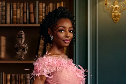 Venita Aspen wearing a pink dress standing in front of a book shelf