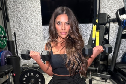 Dolores Catania wearing a black sports bra and black shorts lifting weights in a gym