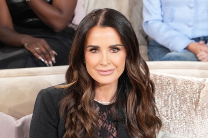 Kyle Richards smiling while sitting on a sofa.