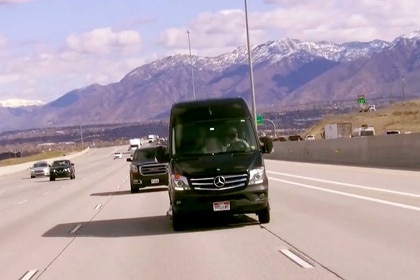 A black sprinter van driving down a highway in Salt Lake City, Utah with a mountain range behind it