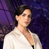 Katie Maloney wearing a white jacket with a black tank top in a purple room overlooking LA.