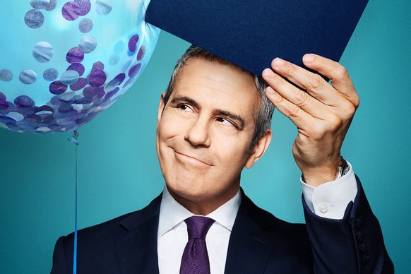 Andy Cohen holding a balloon and note cards in front of a blue backdrop.
