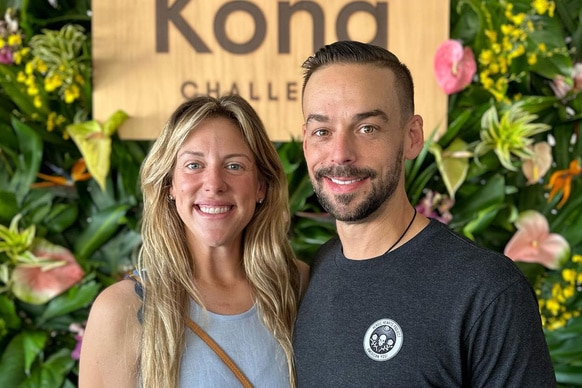 Briana Culberson and Ryan Culberson smiling together in front of a foliage wall.