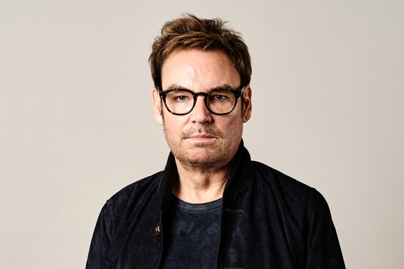 Whitney Sudler Smith wearing a denim jacket and a black tee shirt in front of a beige backdrop