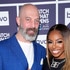 Candiace Dillard Bassett and Chris Bassett smiling in front of a step and repeat at the Watch What Happens Live clubhouse in New York City.