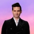 Josh Flagg wearing a black blazer in front of a purple and pink background.