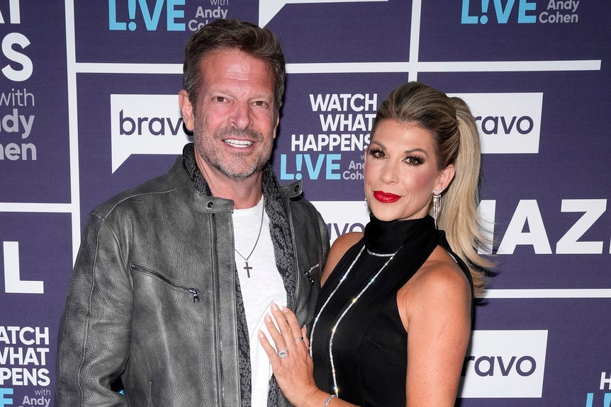 Alexis Bellino and her fiance John Janssen standing in front of the WWHL step and repeat