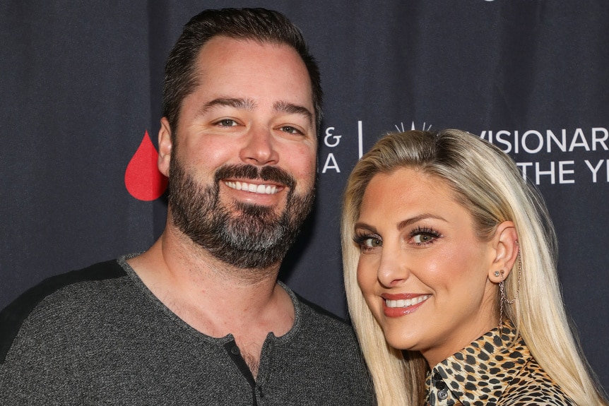 Gina Kirschenheiter and Travis Mullen posing together in front of a step and repeat.